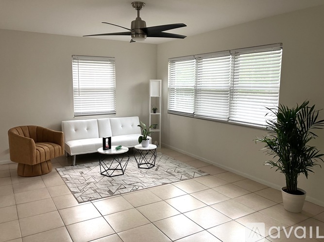 A living room with a white couch, a brown armchair, a ceiling fan, and a potted plant.