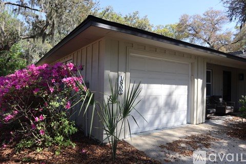 A house with a white garage door and a tree with purple flowers in front.