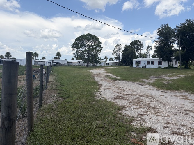 A rural landscape with a dirt road, a fence, and a white building.