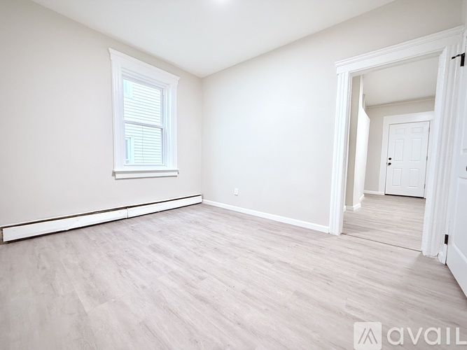 A spacious room with light wood flooring and white walls.