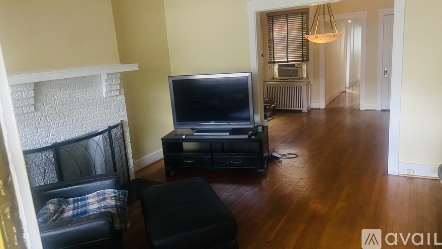 A living room with a television, a black ottoman, and a fireplace.