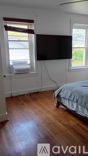 A bedroom with a bed, a window with blinds, and a flat screen TV mounted on the wall.