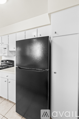 A black refrigerator in a kitchen with white cabinets.