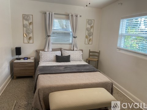 A bedroom with a large bed, a nightstand, and a window with curtains.