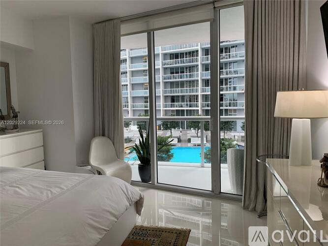 A bedroom with a large bed, a chair, and a view of a pool and buildings outside.