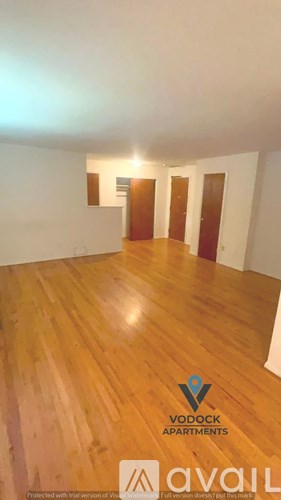 A room with wooden flooring and white walls, with a logo for Vodock Apartments in the bottom right corner.
