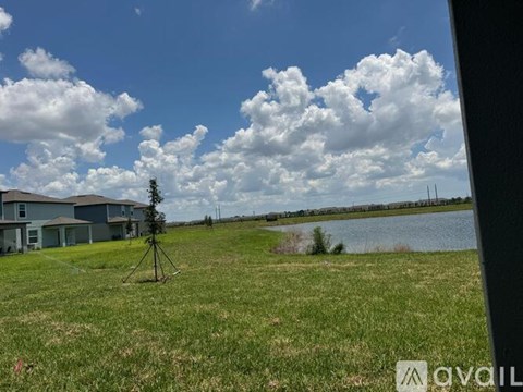 A grassy field with a lake and houses in the background.