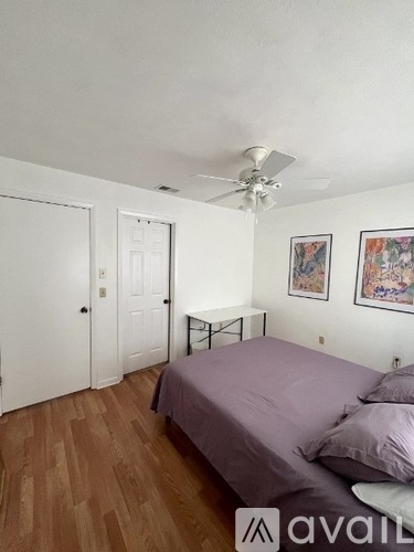 A bedroom with a bed, a ceiling fan, and two pictures on the wall.