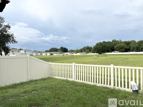 A white picket fence in a grassy area with houses in the background.