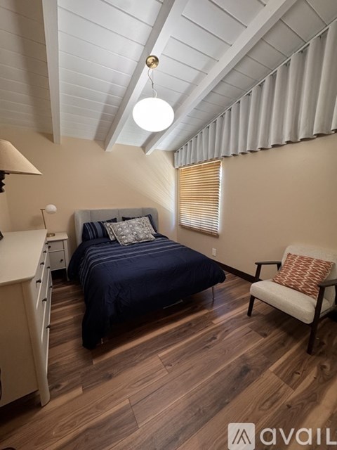 A bedroom with a bed, chair, and wooden floors.