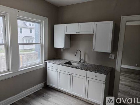 A kitchen with white cabinets and a window overlooking a house.