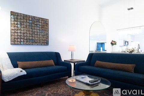 A living room with a blue couch, a glass table, and a large painting on the wall.