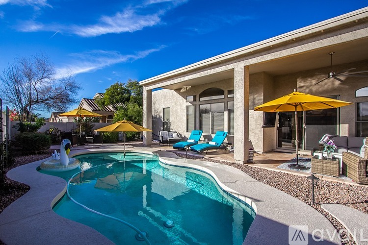 A swimming pool in a backyard with a yellow umbrella and blue chairs.