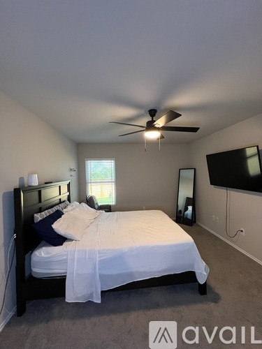 A bedroom with a bed, a ceiling fan, and a flat-screen TV mounted on the wall.