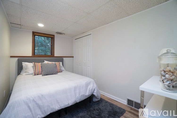 A bedroom with a bed, a nightstand with a lamp, and a window with a view of trees.