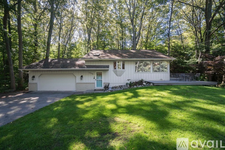 A house with a white exterior and a brown roof is surrounded by trees.