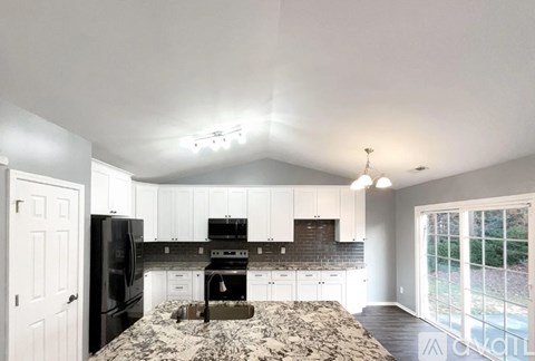A kitchen with black appliances and a black and white marble countertop.