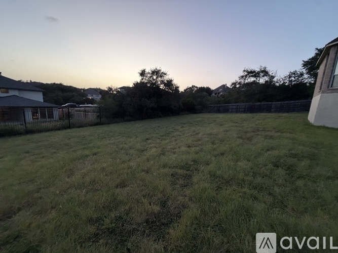 A grassy field with a house and trees in the background.