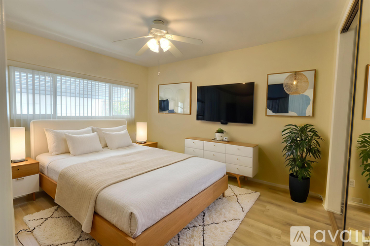 A bedroom with a large bed, a ceiling fan, and a TV mounted on the wall.