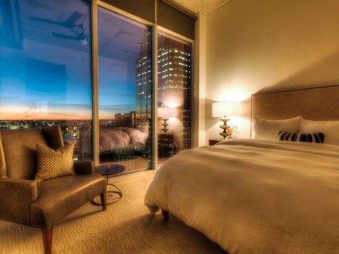 A well-lit bedroom with a large bed and a view of the cityscape outside.
