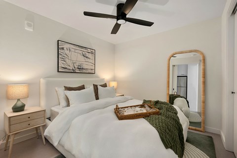 A bedroom with a large bed, a ceiling fan, and a mirror.