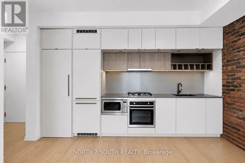 A white kitchen with a brick wall behind it.