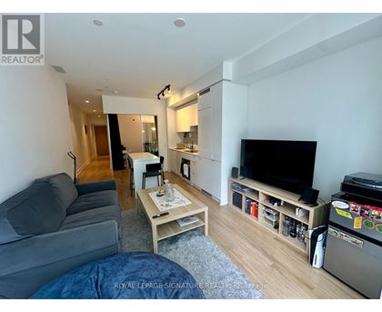 A living room with a grey couch, a wooden coffee table, a flat screen TV, and a refrigerator.