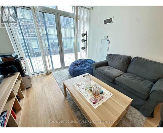 A living room with a grey couch, a coffee table with a map on it, and a large window with a view of a building outside.