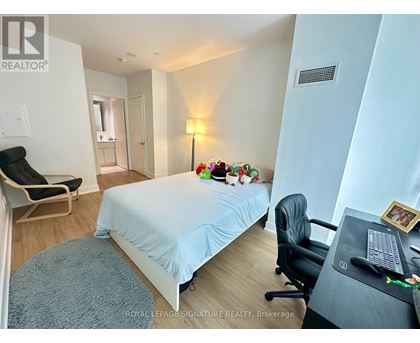 A bedroom with a bed, desk, chair, and a lamp.