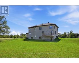 A large house with a balcony is situated on a grassy hill.
