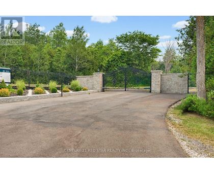 A driveway leads to a gated entrance with a brick pillar on either side.