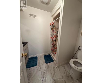 A white bathroom with a toilet, a marble floor, and a shower with a floral curtain.