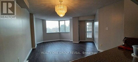 A large, empty room with a chandelier and a window overlooking a tree-covered landscape.
