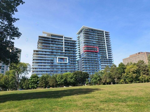 A modern glass building with a red stripe on the side stands tall in a park.