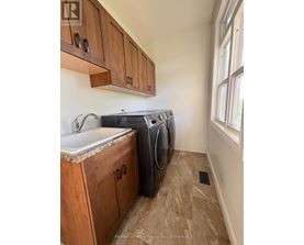 A laundry room with a sink, cabinets and a window.