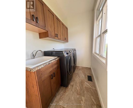 A laundry room with a sink, cabinets and a window.