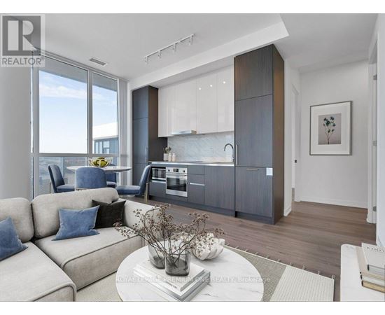 A modern living room with a large window and a kitchen area in the background.
