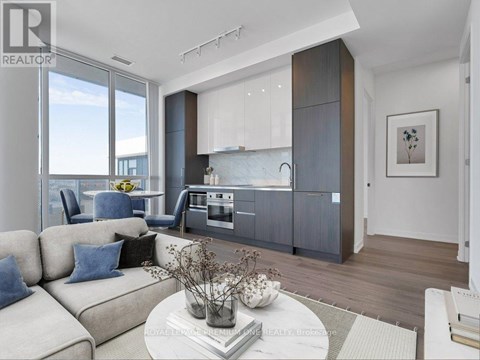 A modern living room with a large window and a kitchen area in the background.