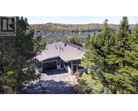 A house with a brown roof is surrounded by trees and has a lake in the background.