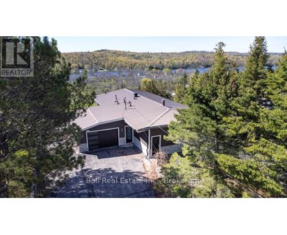 A house with a brown roof is surrounded by trees and has a lake in the background.
