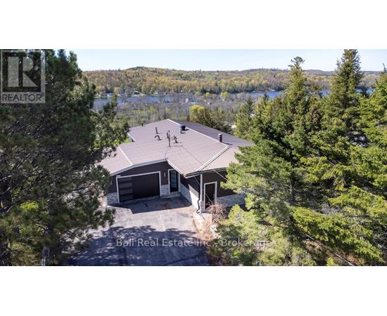 A house with a brown roof is surrounded by trees and has a lake in the background.