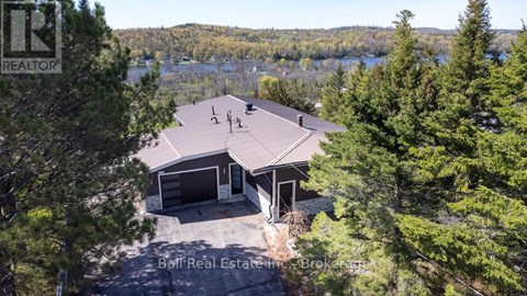 A house with a brown roof is surrounded by trees and has a lake in the background.