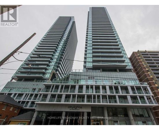 Two tall buildings with glass windows and balconies are in front of a cloudy sky.