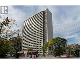 A tall building with a glass facade stands in front of a tree with autumn leaves.