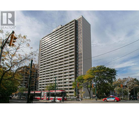 A tall building with a glass facade stands in front of a tree with autumn leaves.