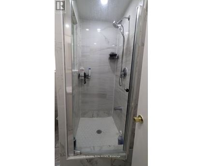 A shower with a glass door and a marble floor.