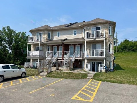 A white car is parked in a parking lot in front of a two-story apartment building.