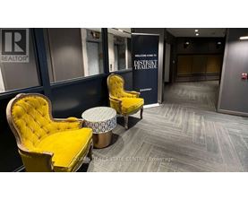 A yellow chair with a matching ottoman is in the foreground of an office lobby.