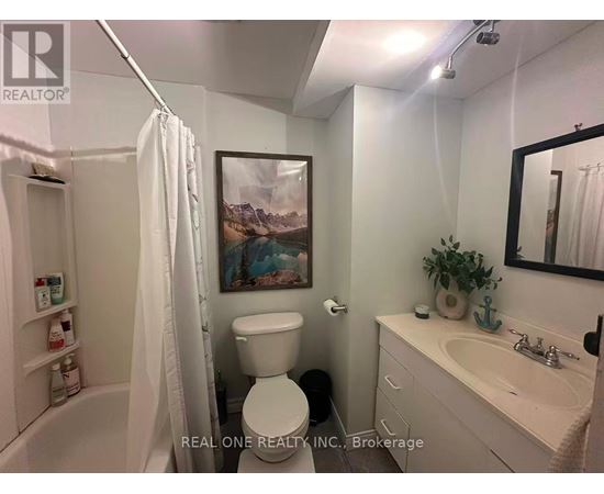A white bathroom with a toilet, sink, and a painting on the wall.