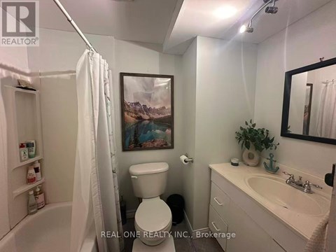 A white bathroom with a toilet, sink, and a painting on the wall.